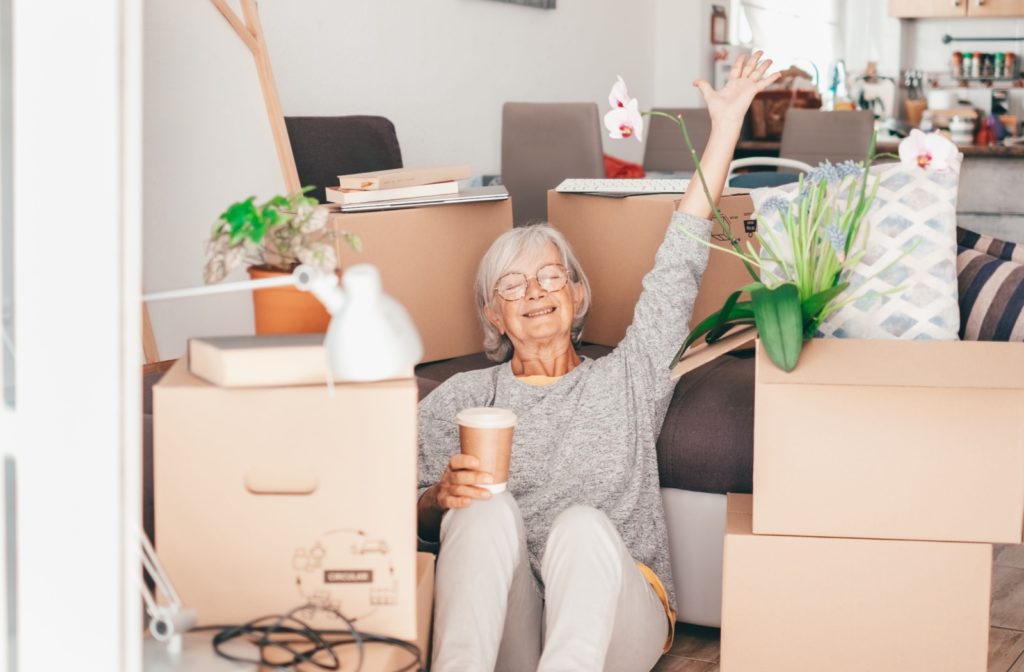 A happy senior sitting in front of her moving boxes with a coffee, celebrating a smooth transition to senior living after effectively downsizing.