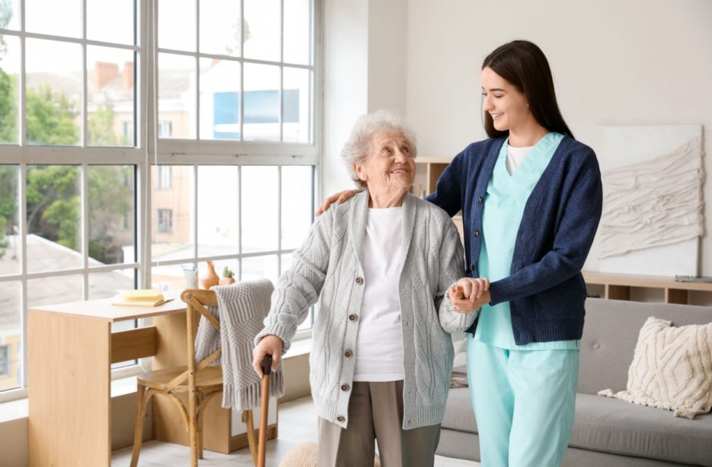 A female caregiver supporting an elderly woman as uses a walking stick to move around.