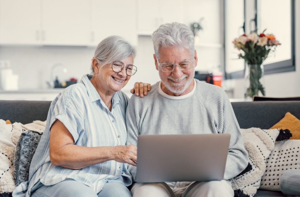 A senior couple smiles while using a laptop to research independent living communities to find one that fits their lifestyle