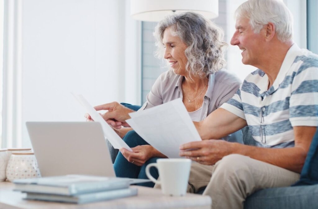 An older couple holds paperwork at their coffee table while researching potential senior living communities together