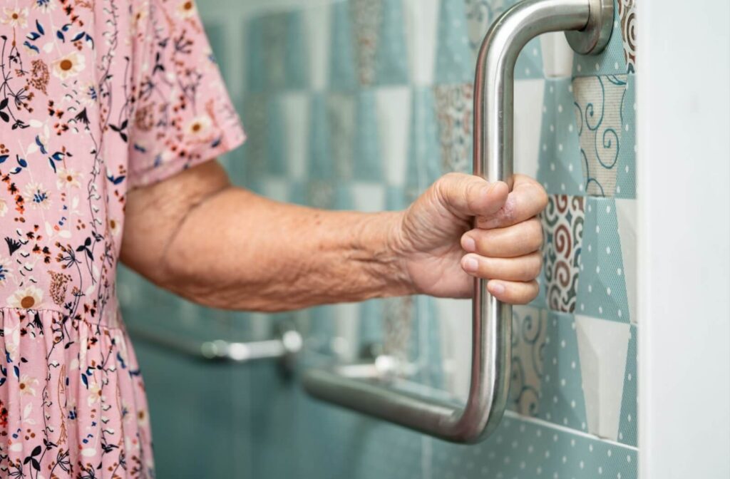 An older adult grabs a curved metal bar in their blue-tiled bathroom to safely navigate their home